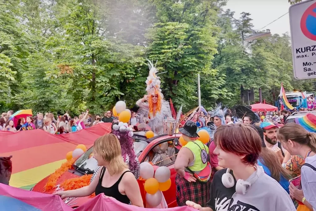Bild auf 5min.at zeigt die CSD-Parade in graz. Es sind mehrere Personen mit Regenbogenfahnen zu sehen.
